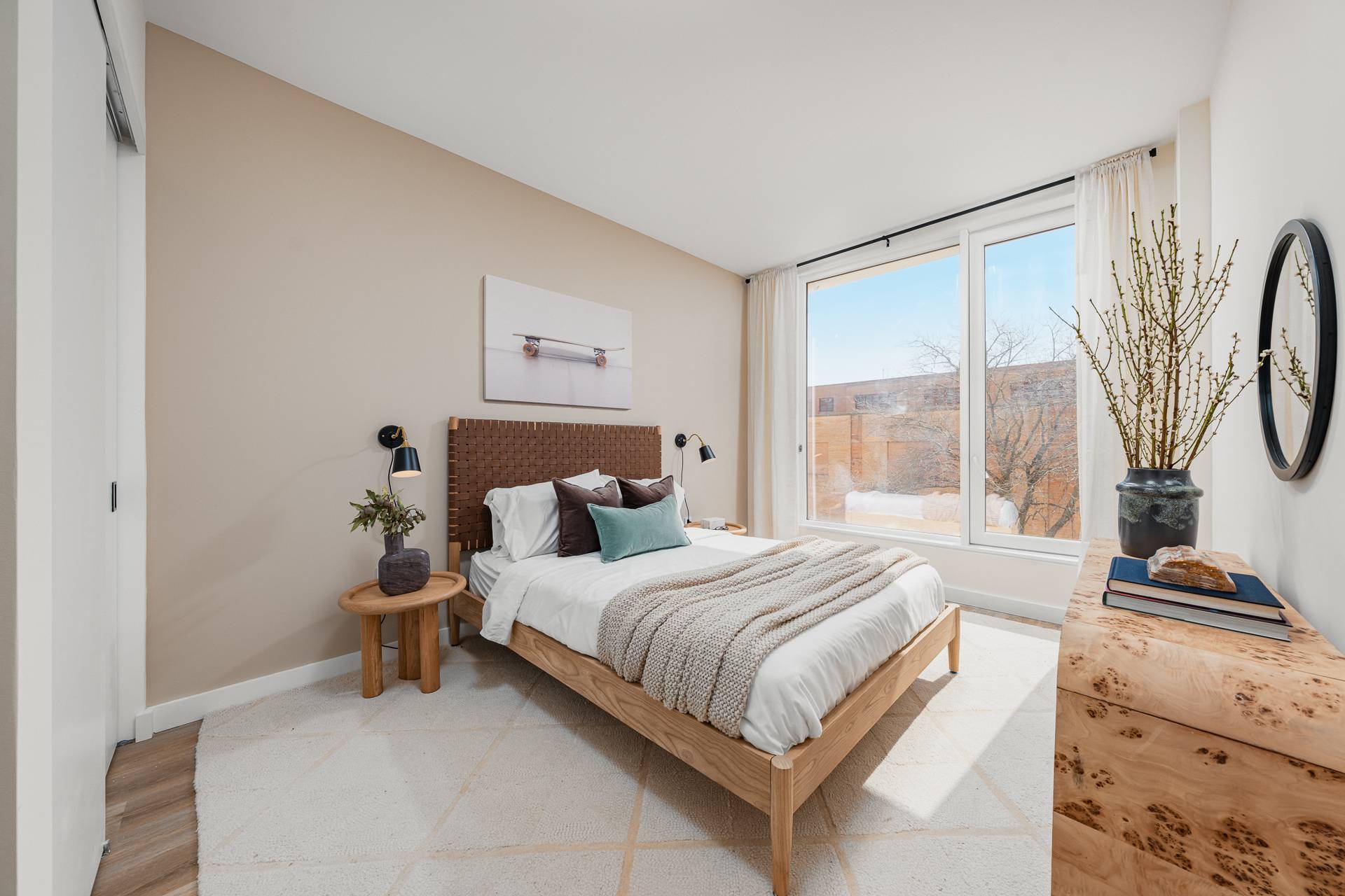 bright modern bedroom with wood tone furniture, rug on wood floors and large window