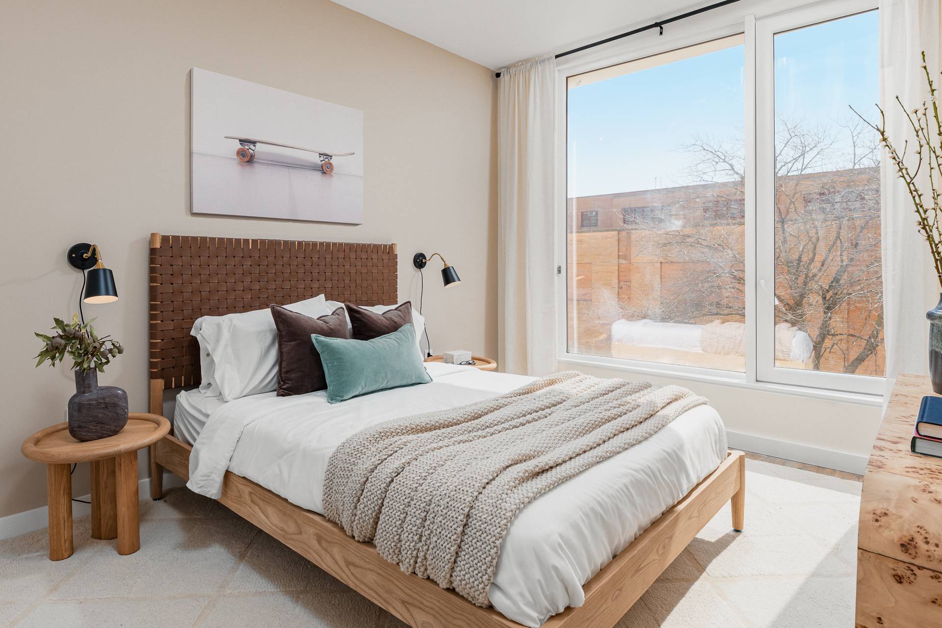 bright modern bedroom with wood tone bed and nightstands on a rug on wood floors and large window to the side